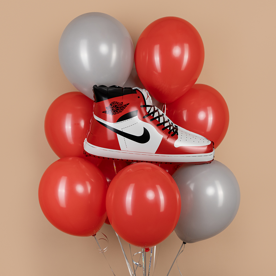Воздушный шар в форме красных кроссовок Nike среди красных и серых шаров.